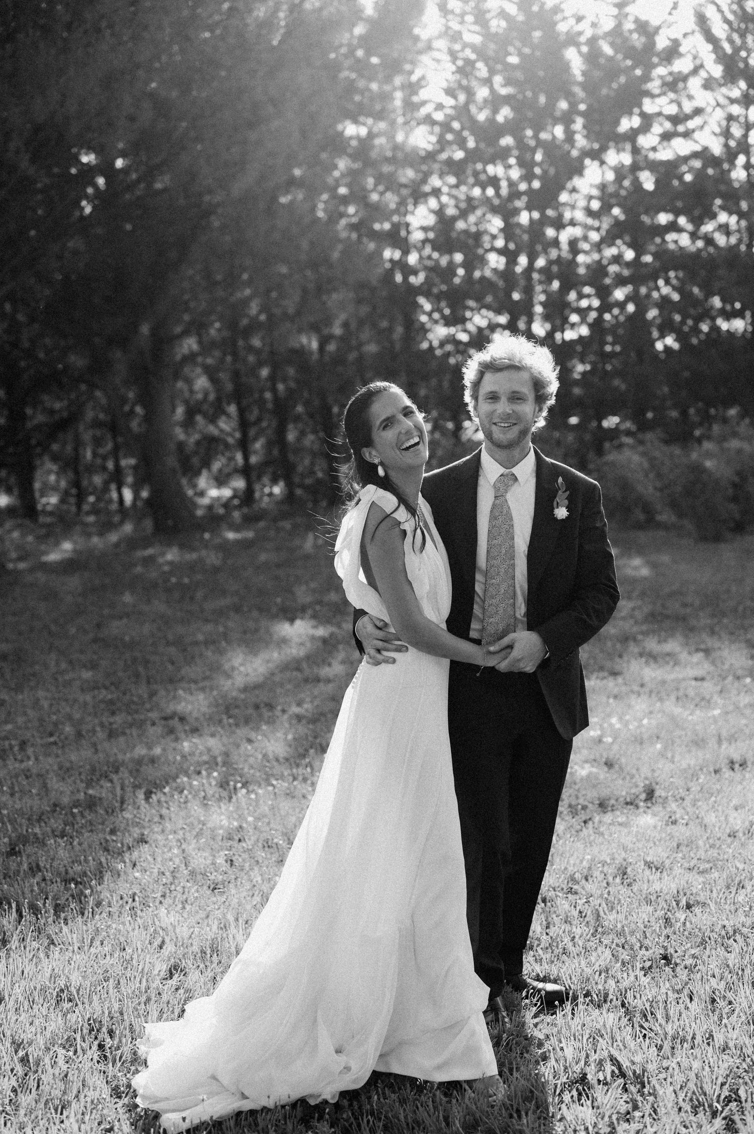 A romantic wedding couple dances and twirls in a sunlit meadow wearing formal attire.