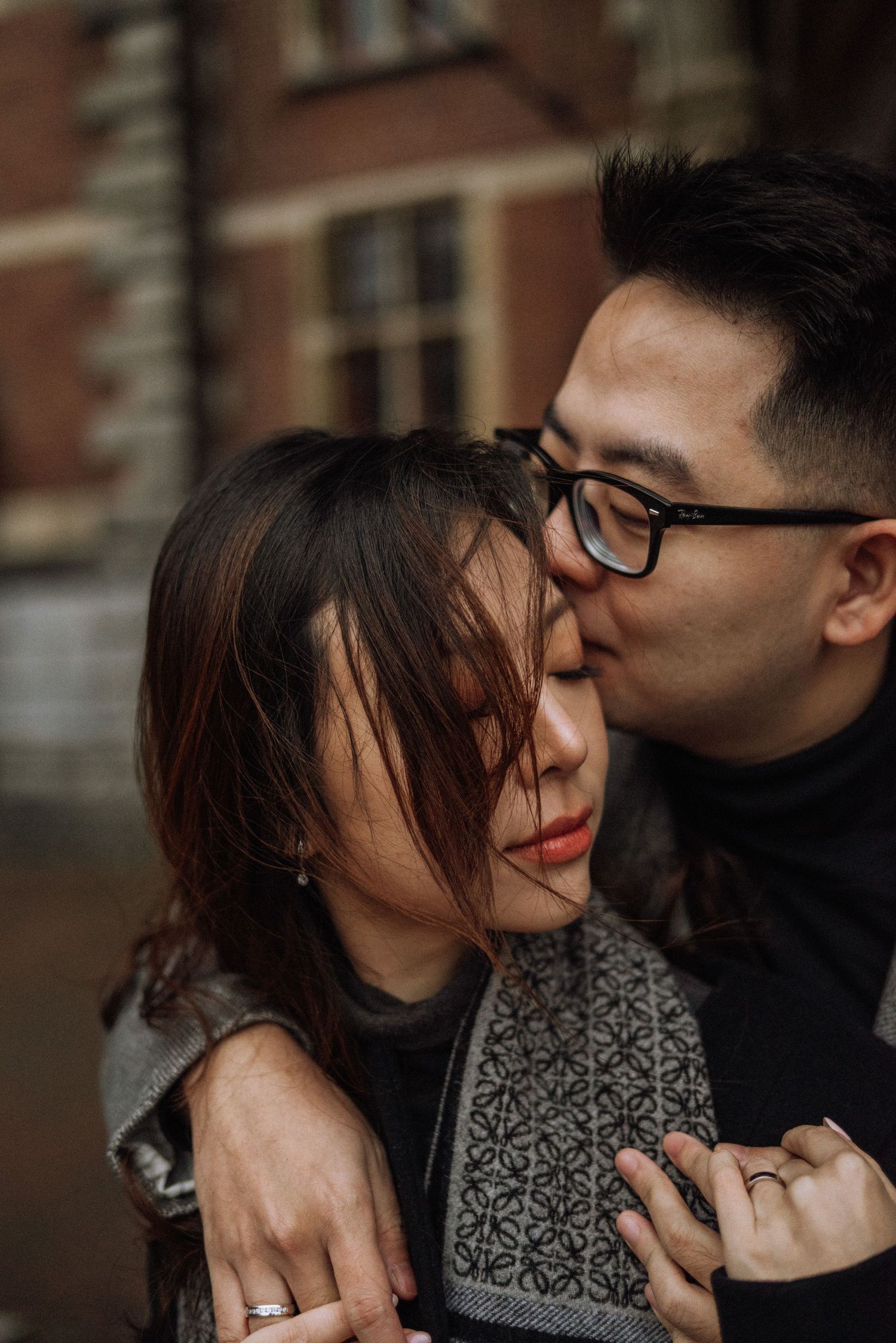 Intimate romantic moment shared between couple against brick building backdrop.