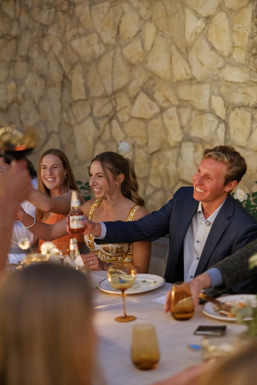 Intimate dinner gathering with candlelight and wine glasses against a stone wall.