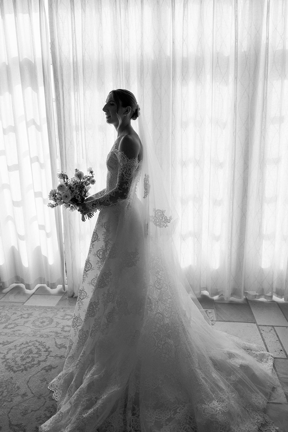 Ethereal silhouette of a bride in a lace wedding dress against backlit white curtains.
