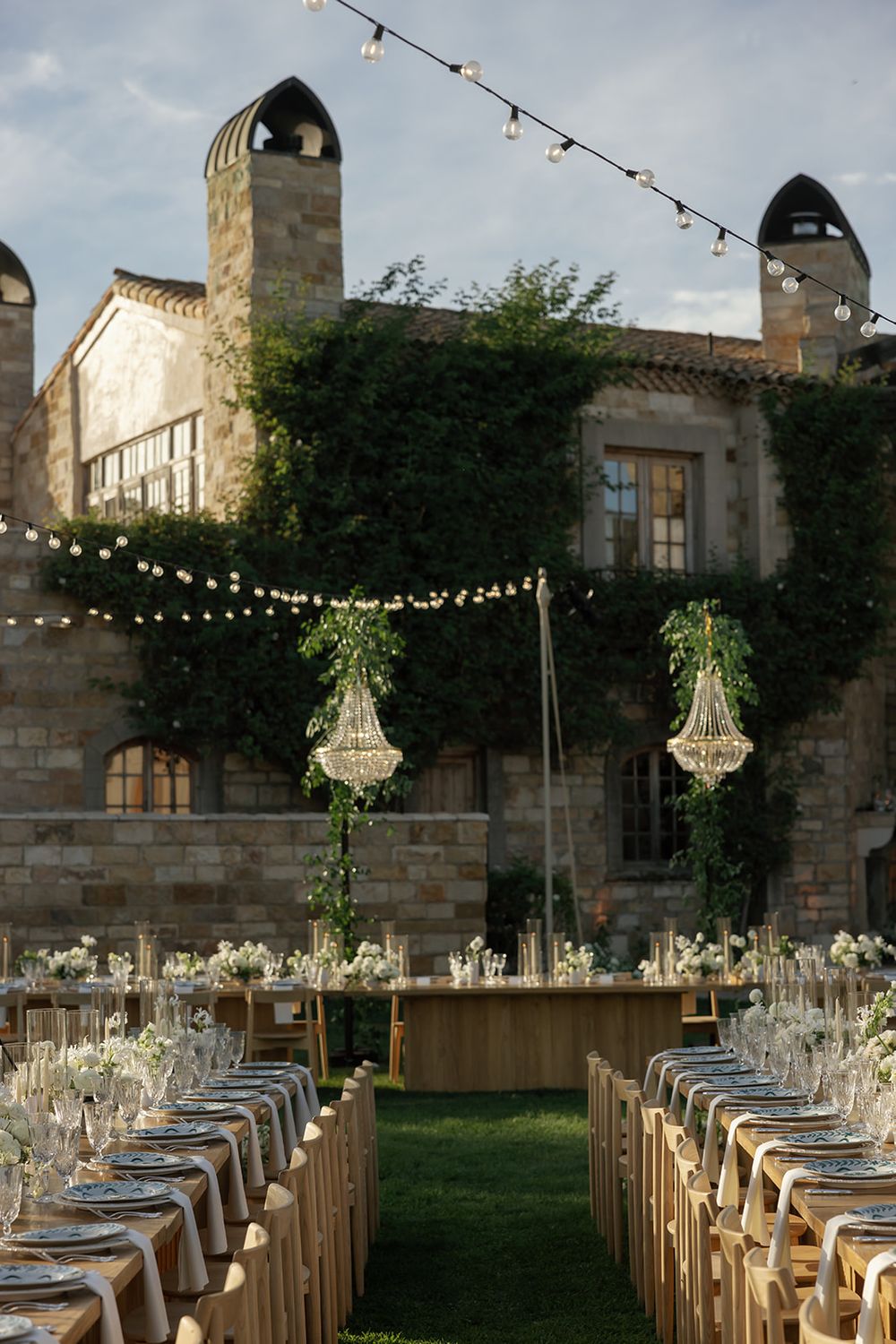 Outdoor wedding reception with string lights and chandeliers between stone villa towers.