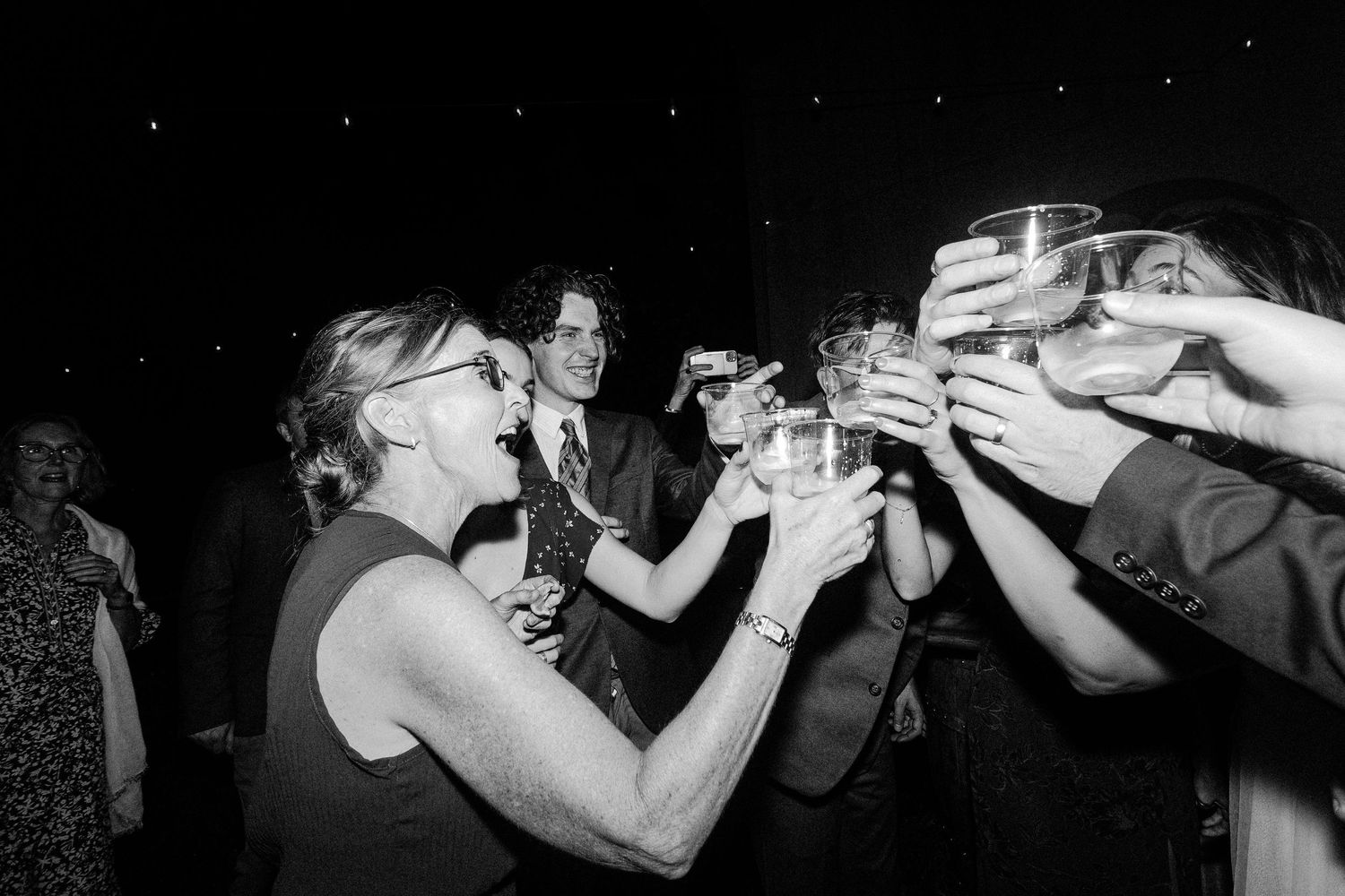 Black and white photo of a celebratory toast with multiple raised glasses. Documentary photographer