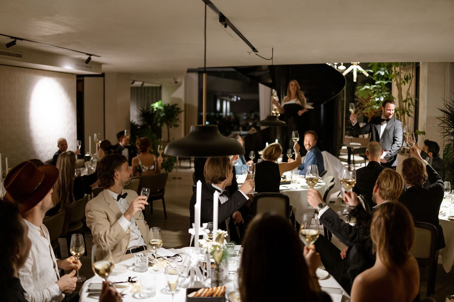 Candlelit dinner party with multiple guests seated at long tables in an elegant dining room.