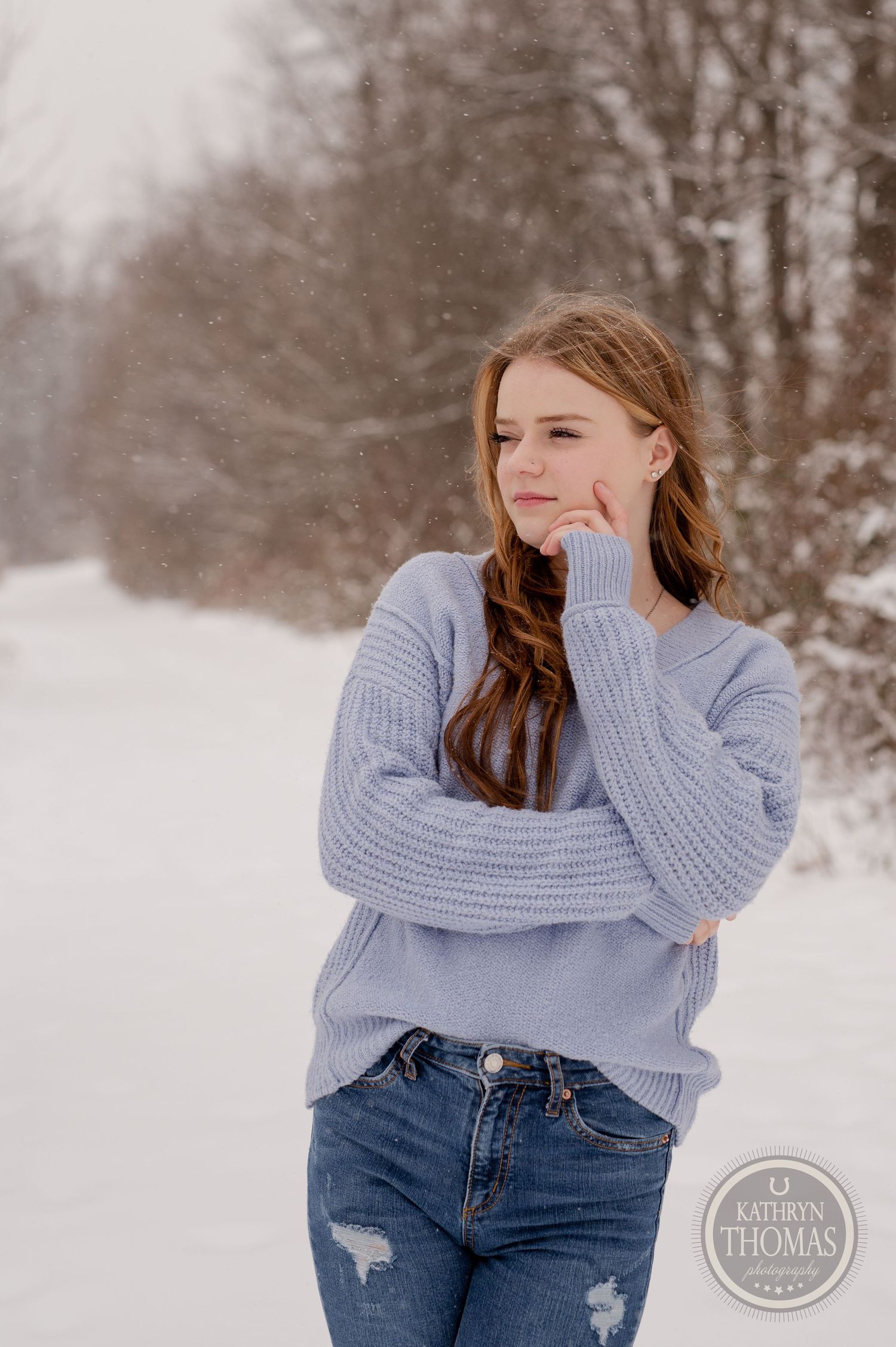 Winter fashion photo featuring a light blue knit sweater and distressed jeans against a snowy forest backdrop.