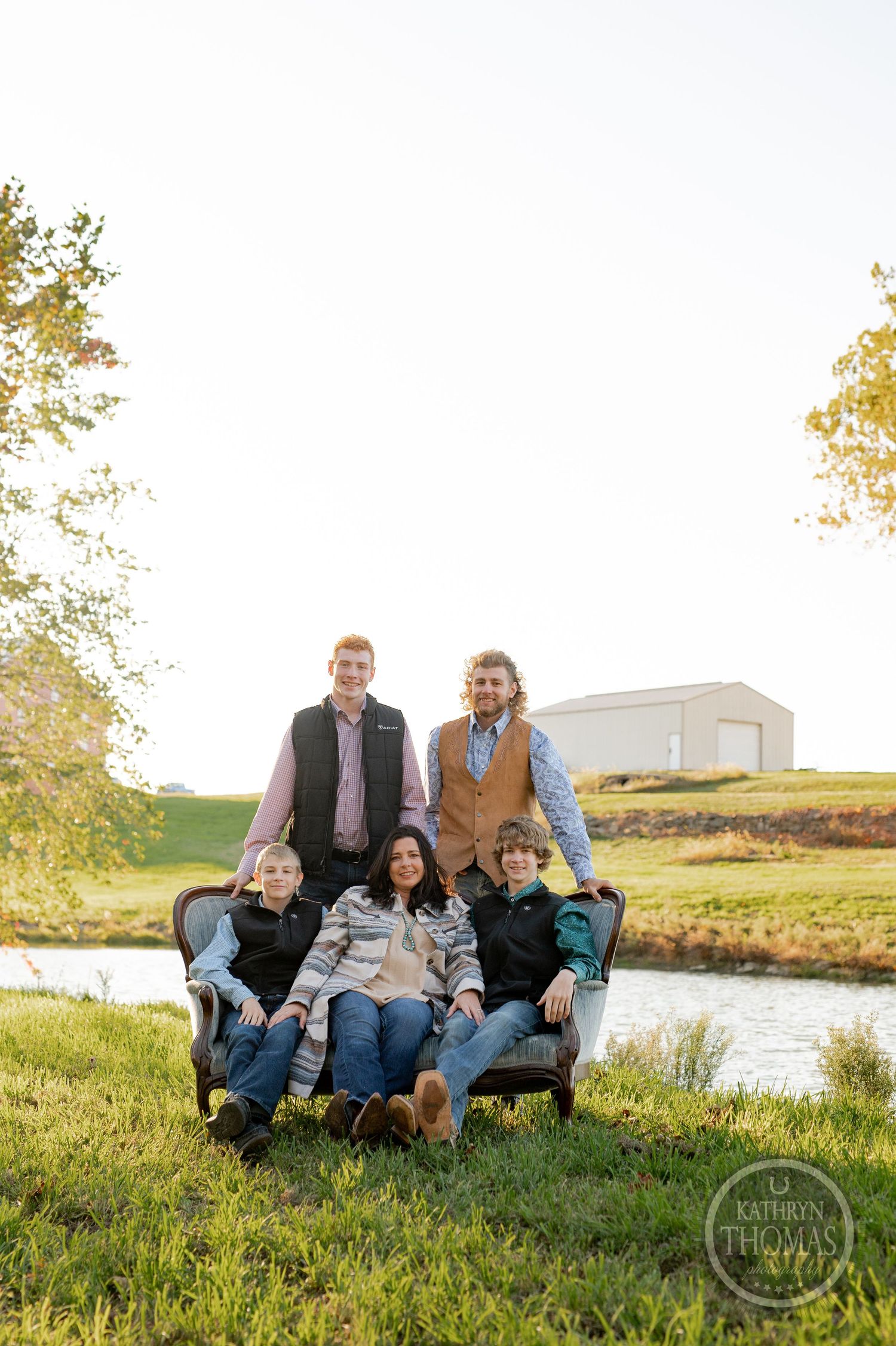 Family group lounging together on a couch outdoors by a pond during golden hour sunset.