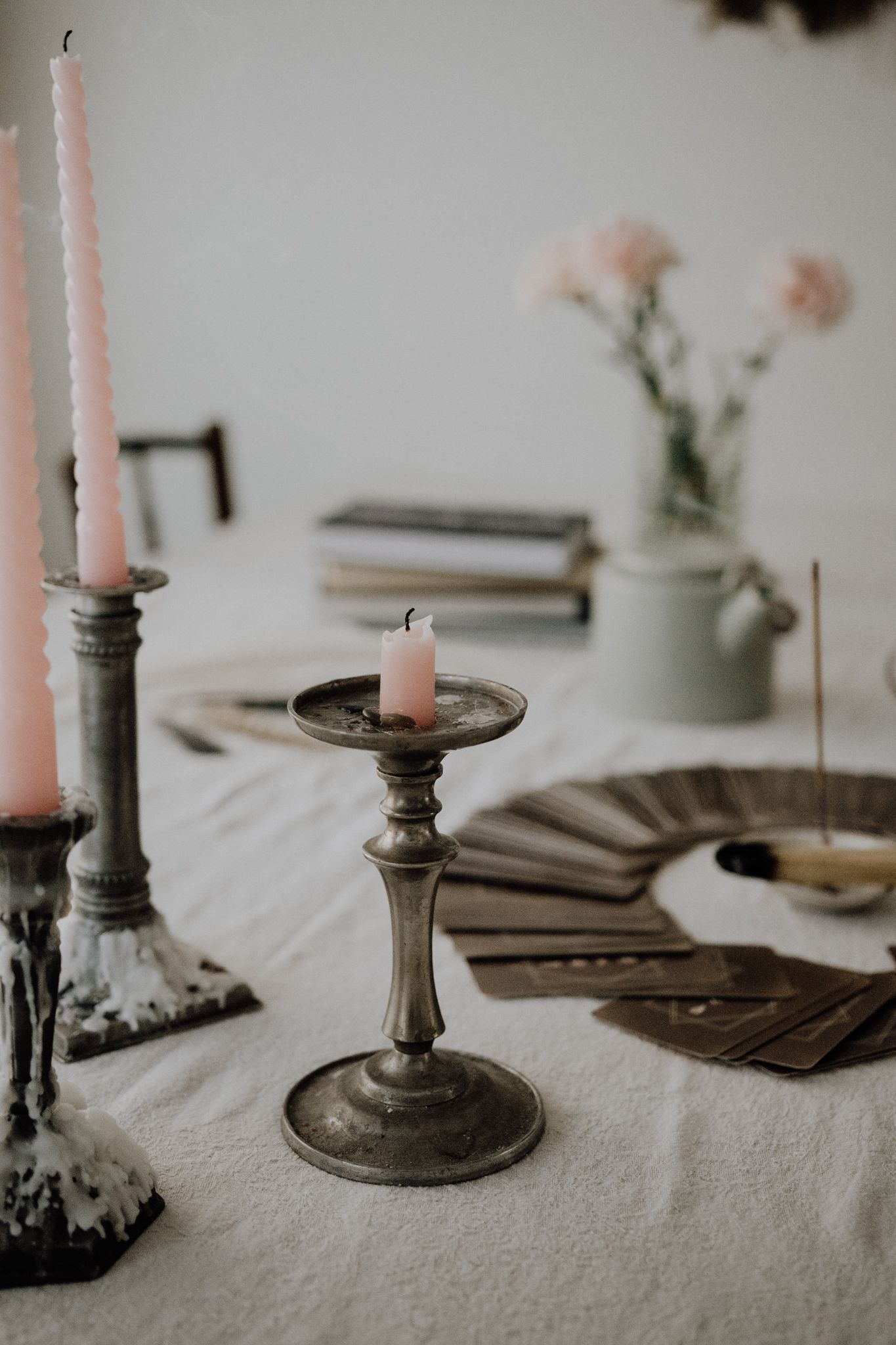 A lit white candle in a ceramic holder with wisps of smoke from burning incense on a dark plate nearby.