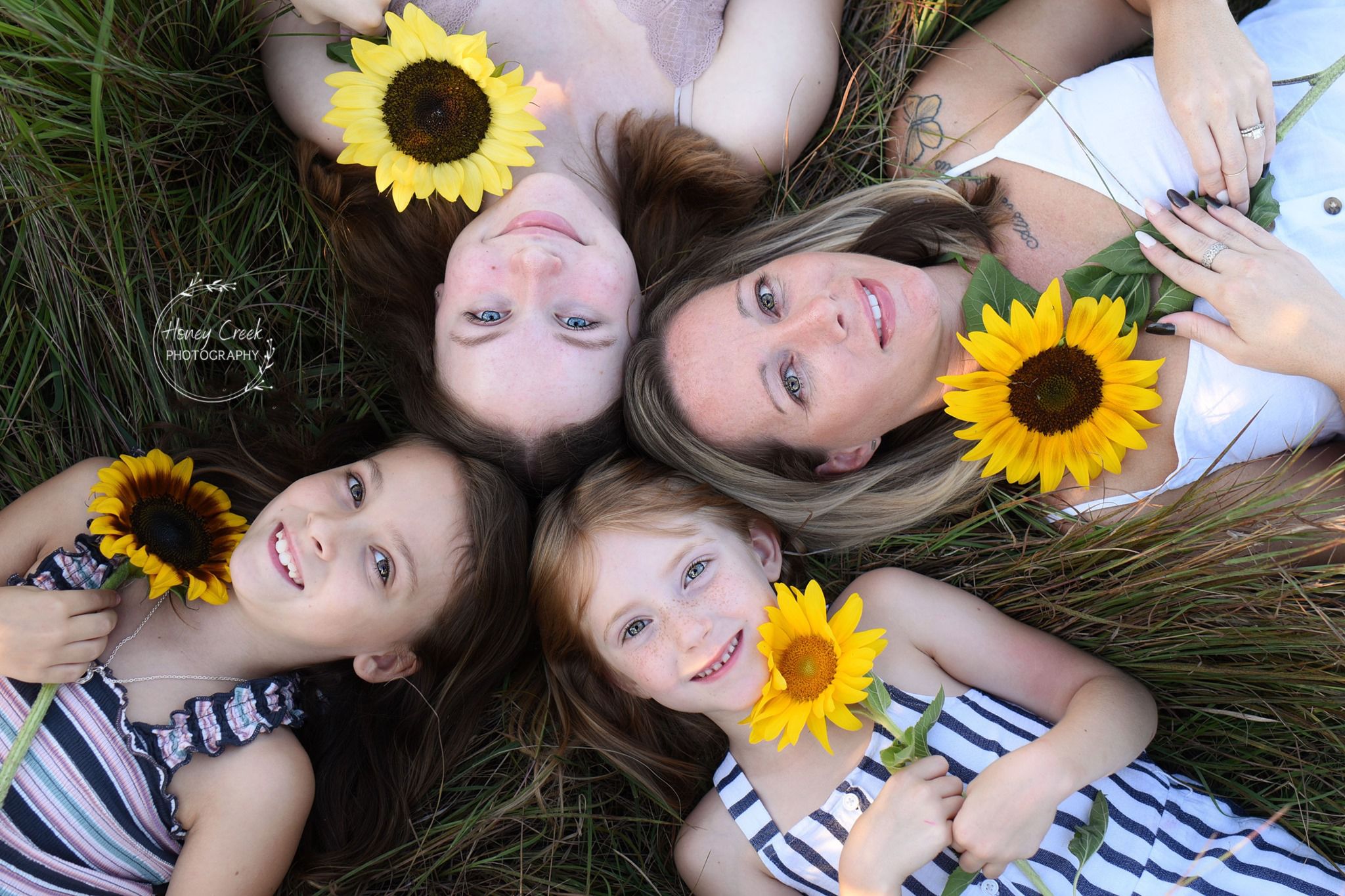 Two people lying in grass wearing striped shirts and sunflowers in a dreamy summer portrait composition.