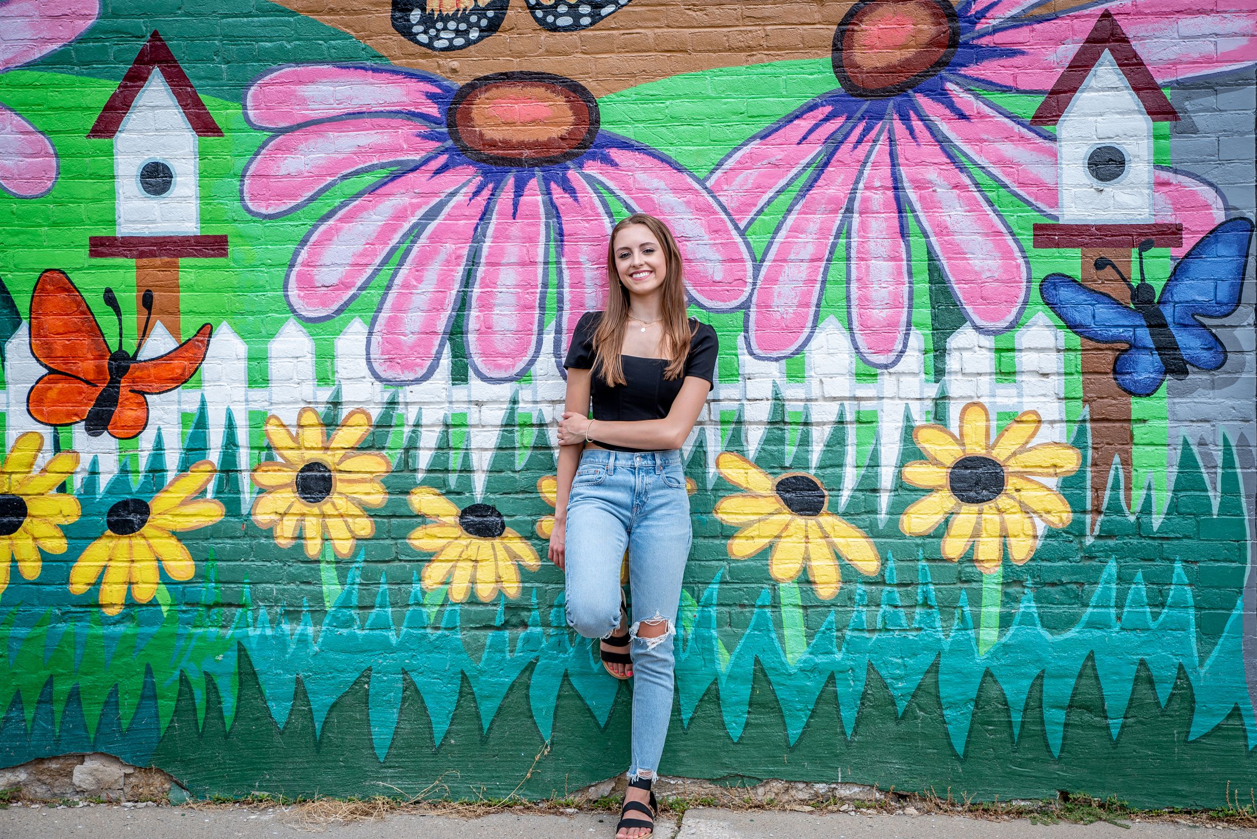 A colorful mural wall with pink daisies, sunflowers, butterflies and birdhouses provides a vibrant outdoor backdrop.