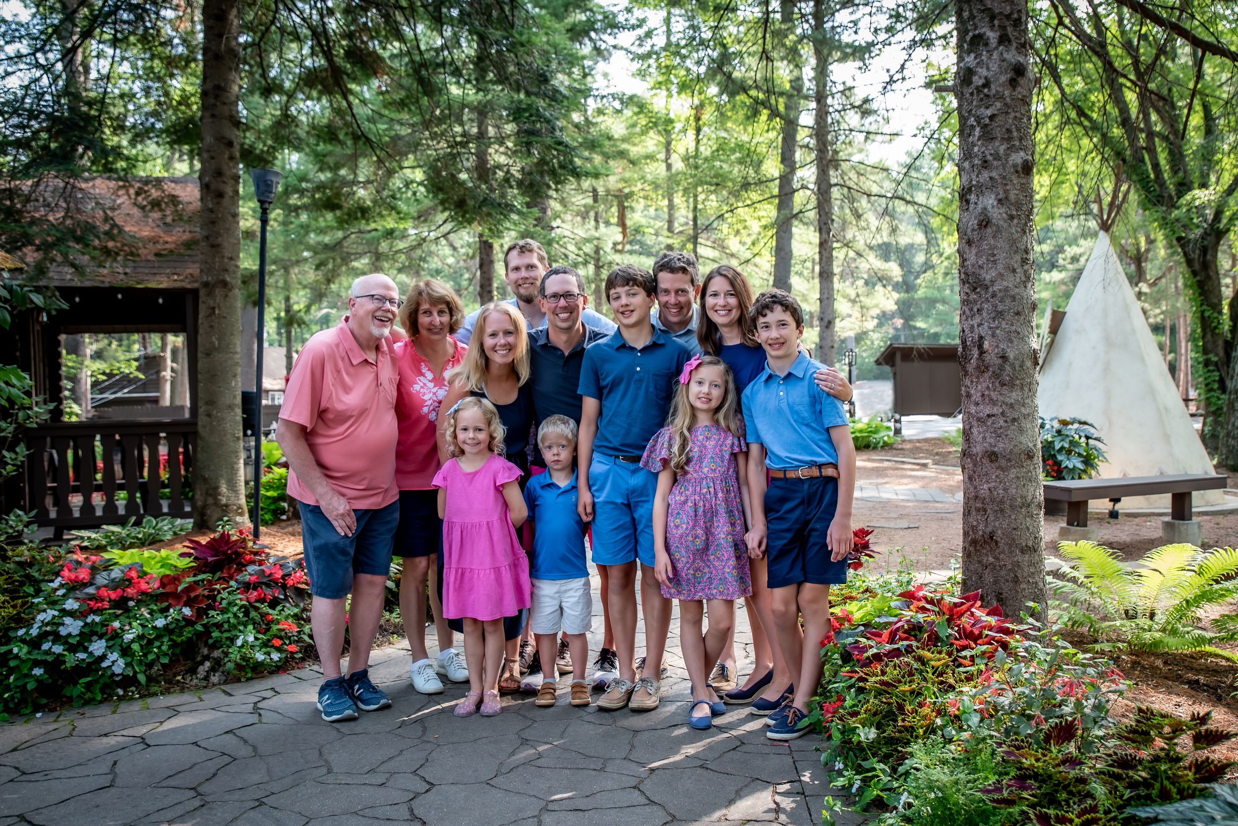 A group in casual attire poses together on a garden path with colorful flowers and trees in the background.