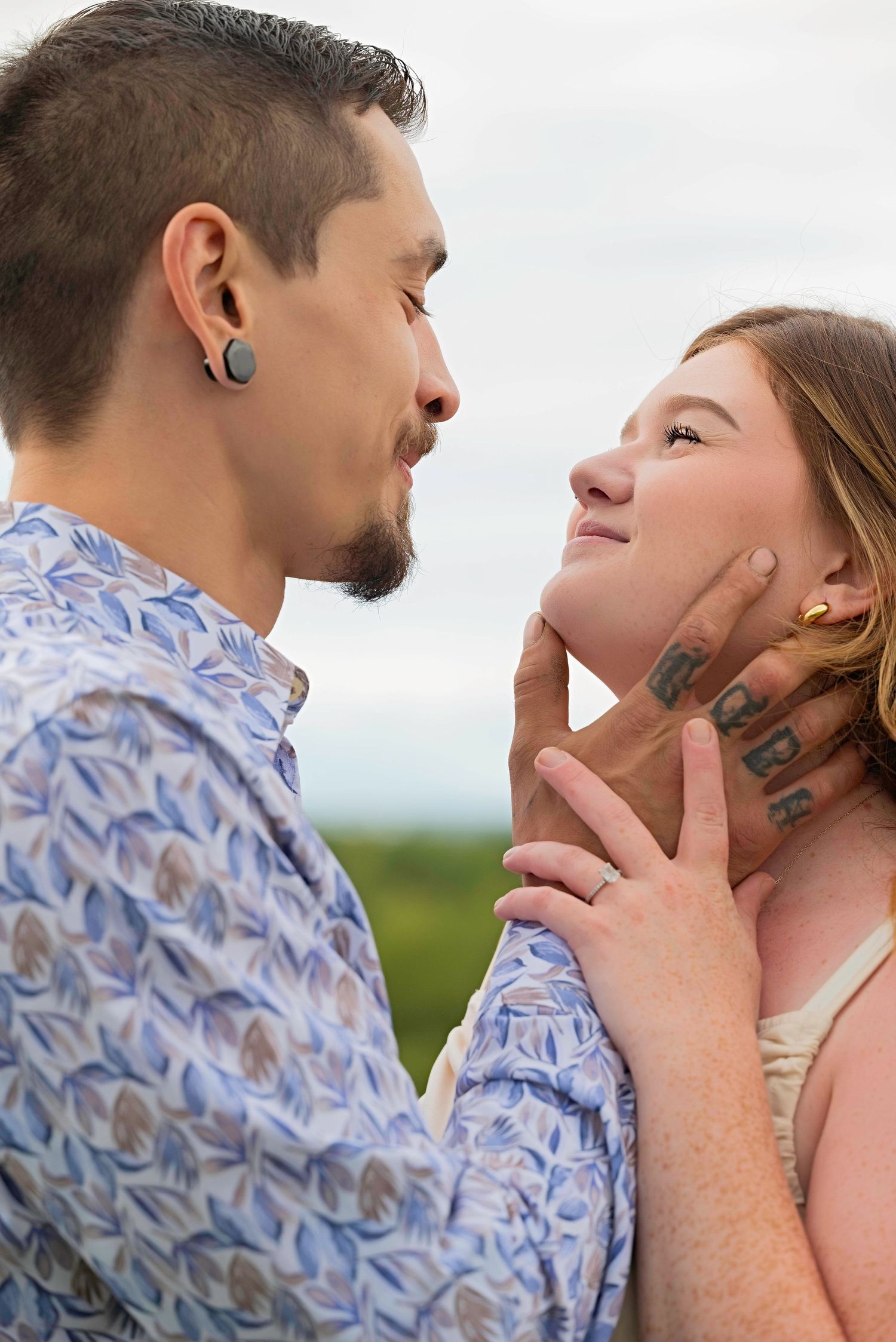 Romantic couple in an outdoor setting share tender moments while wearing a blue patterned shirt.