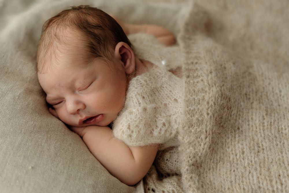 Sleepy newborn covered in neutral blanket