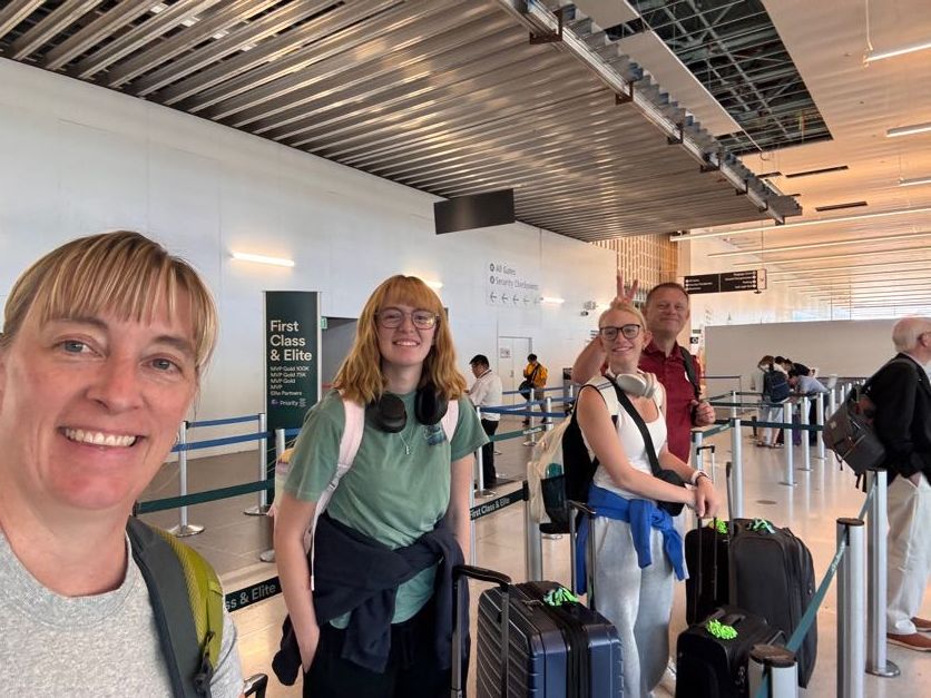 Travel group waiting in line at an airport terminal with luggage and carry-on bags.