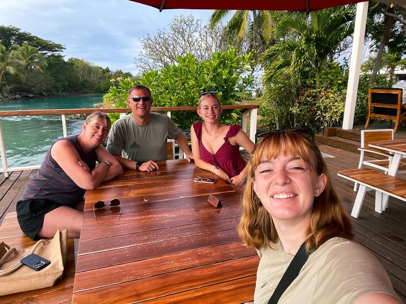 Group enjoying drinks at an outdoor waterfront restaurant table under blue skies.