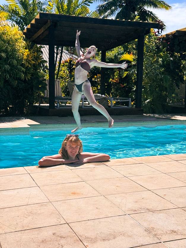 Playful pool scene with someone jumping into bright blue water while another relaxes poolside.