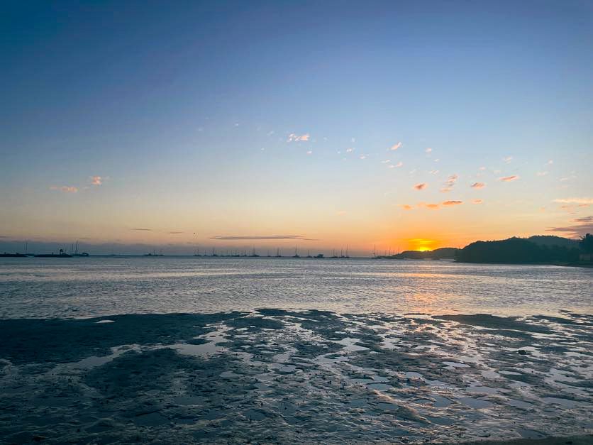 Stunning ocean sunset with bridge silhouette and orange sky reflected on rippling water.
