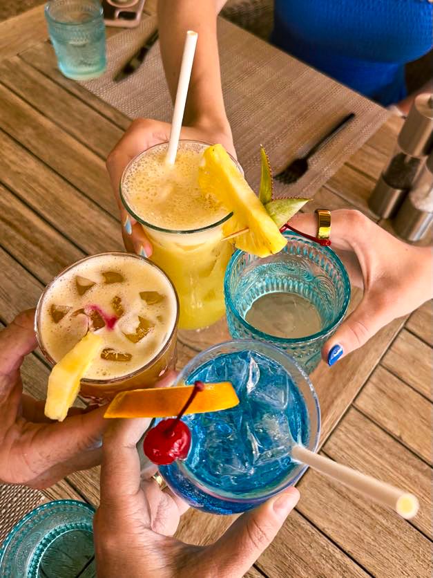 Colorful tropical cocktails with fruit garnishes being held together for a celebratory toast.