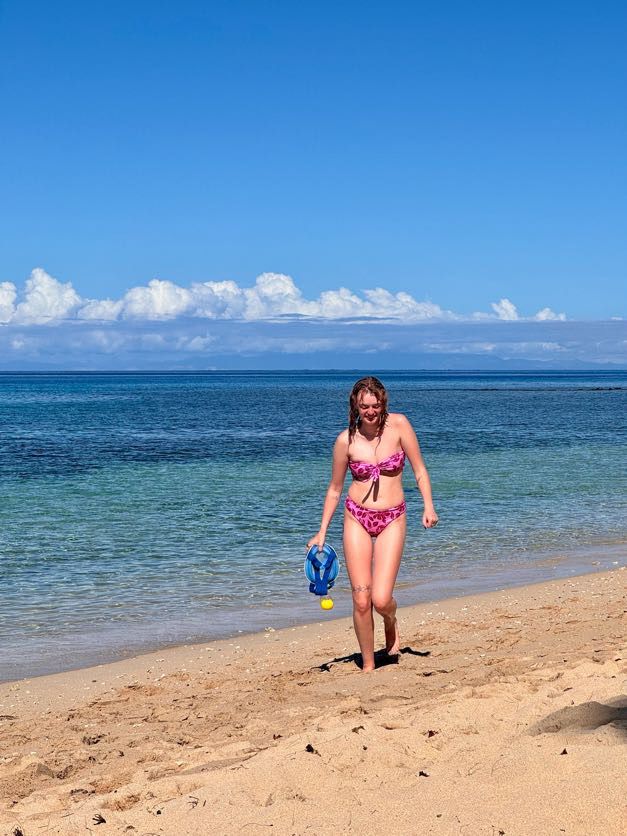 A beachgoer walks along the shoreline on a tropical beach with clear blue water.