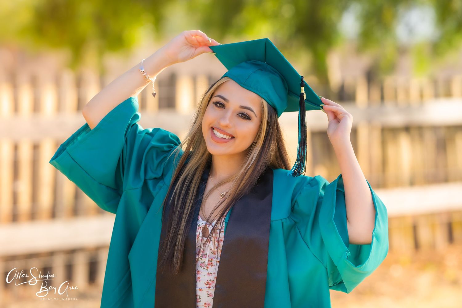 Graduate in emerald cap and gown poses outside during sunny day.