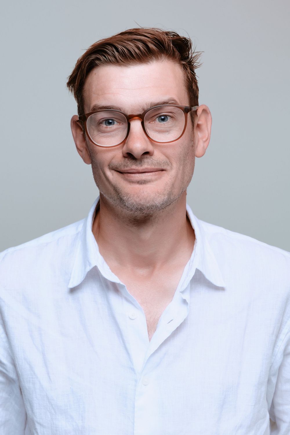 Professional headshot of person wearing glasses and white button-up shirt against gray background.