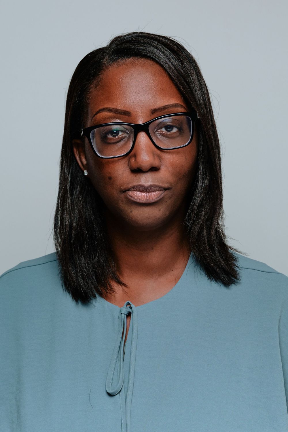 Four close-up studio portraits wearing glasses with a light blue backdrop showing different expressions and angles.