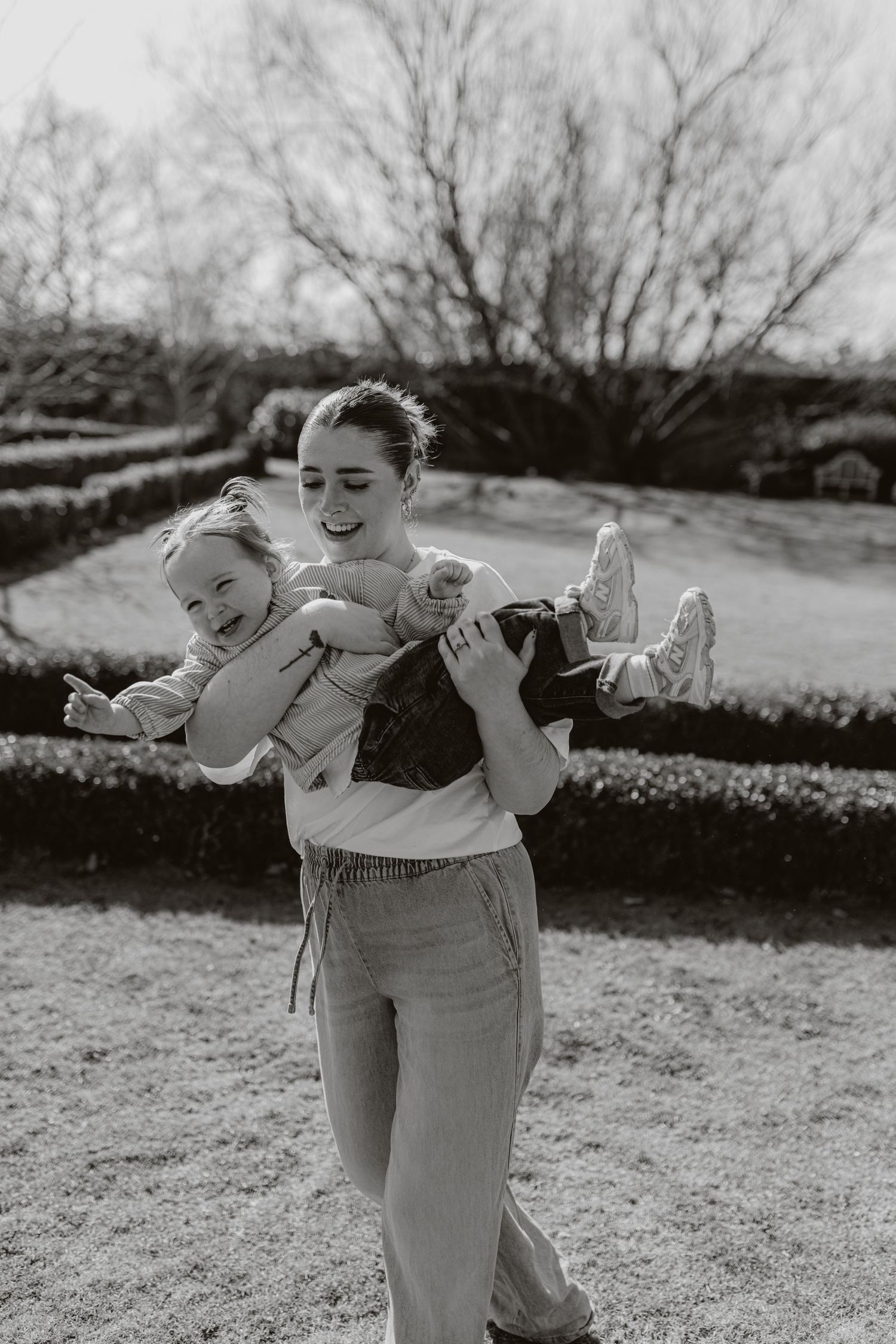 A joyful outdoor moment captured in black and white as a parent playfully lifts a laughing child in the air.
