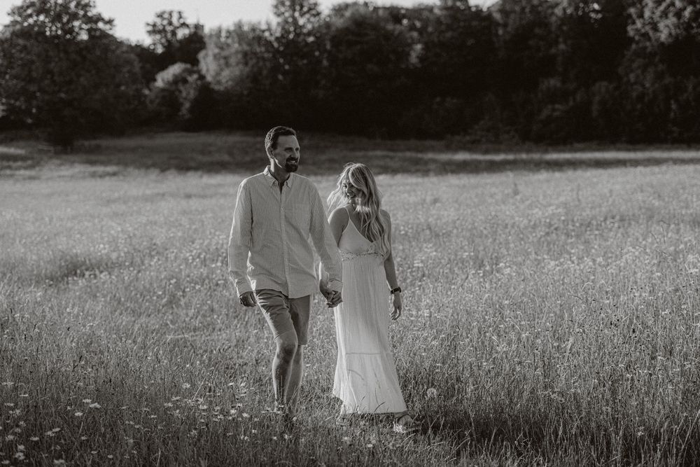 Black and white photo of couple walking hand in hand through meadow in summer.