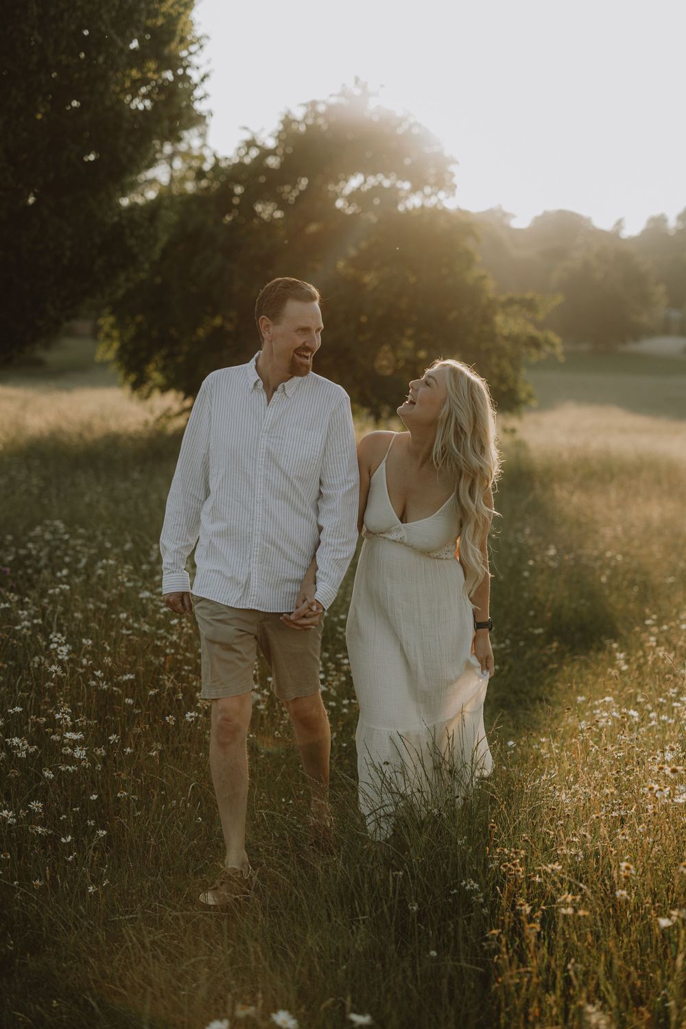 A couple walks hand in hand through a sun-drenched meadow of wildflowers at golden hour.