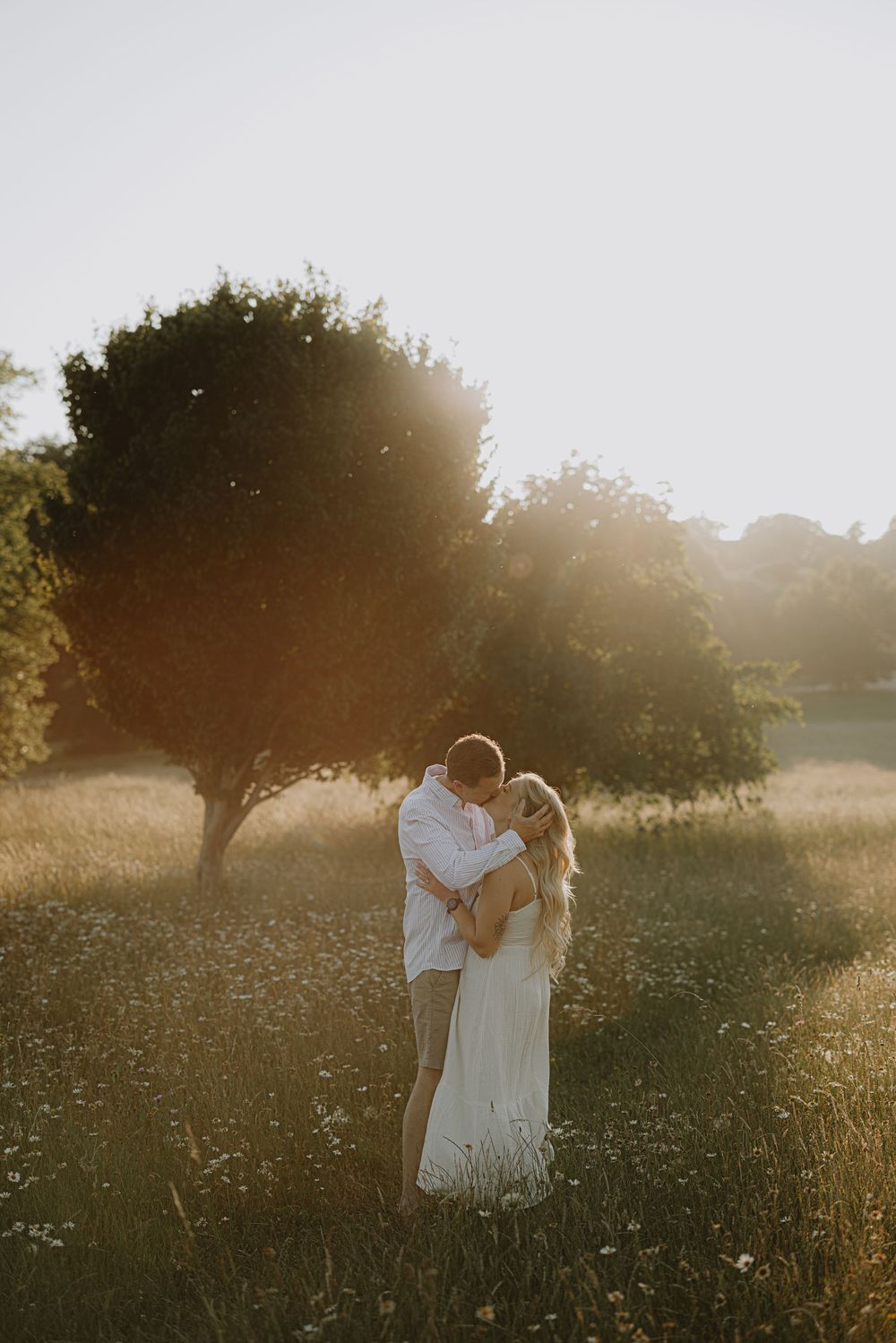 Romantic couple embraces in a sunlit wildflower meadow during golden hour.