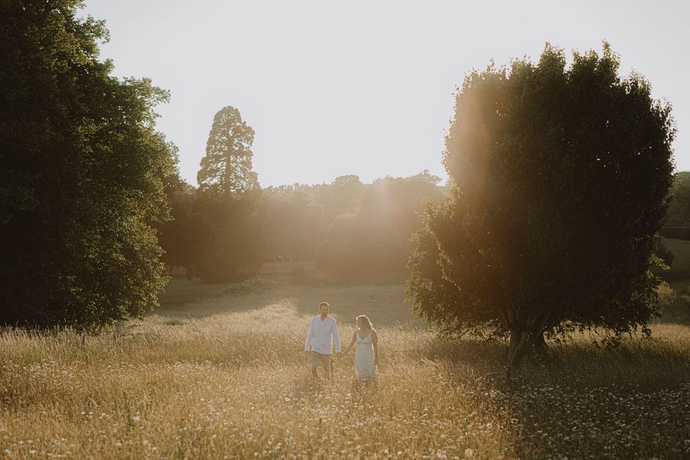 Silhouetted couple walks through sun-drenched field with trees framing the scene.