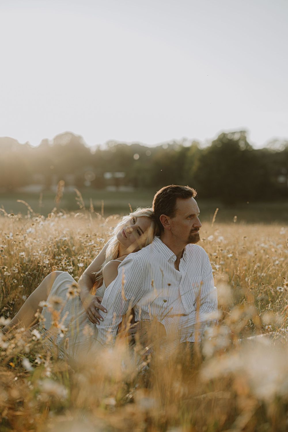 Intimate couple portrait in sunlit field with tall grass and warm evening light.