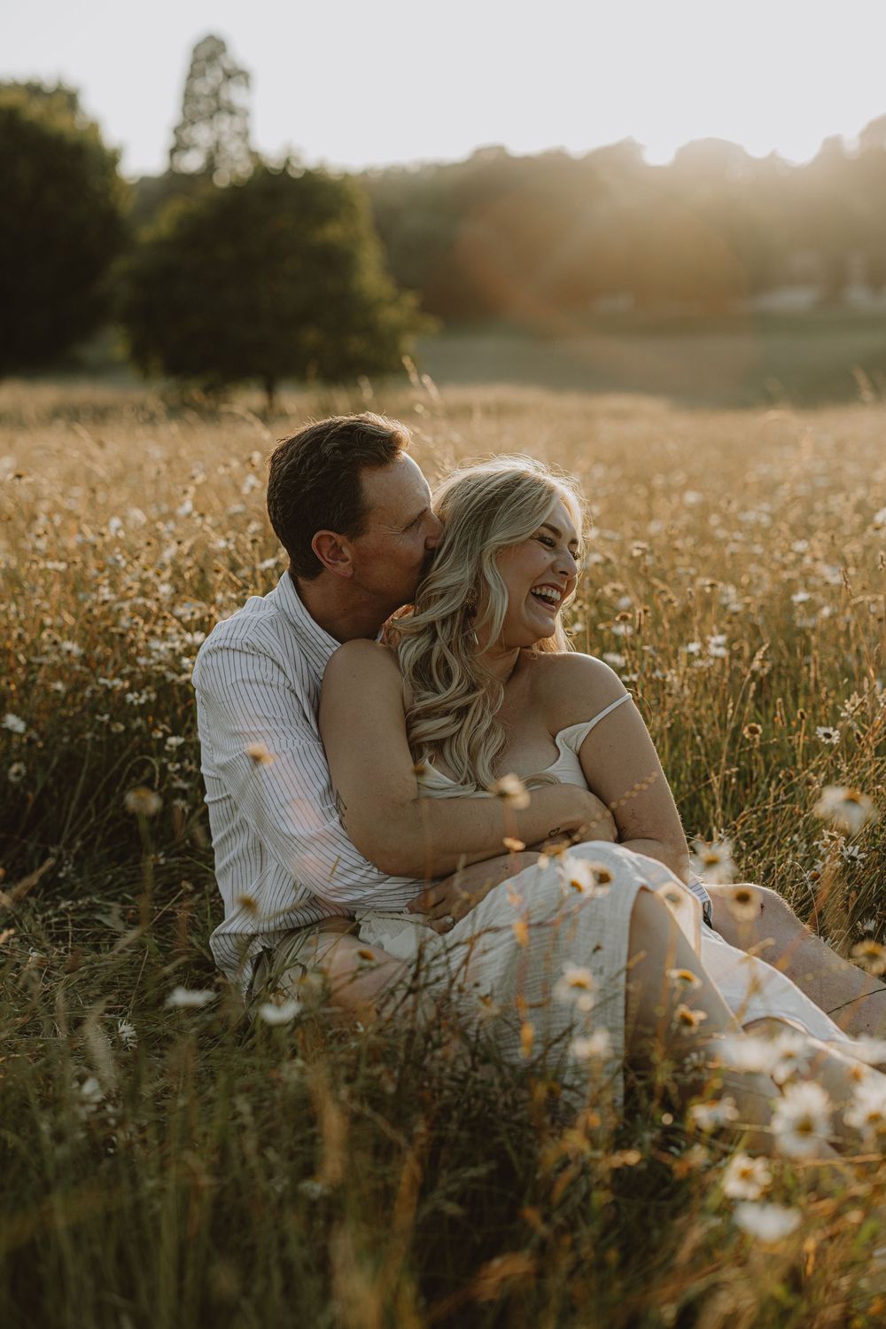 Couple shares loving moment while sitting in wildflower field during golden hour.
