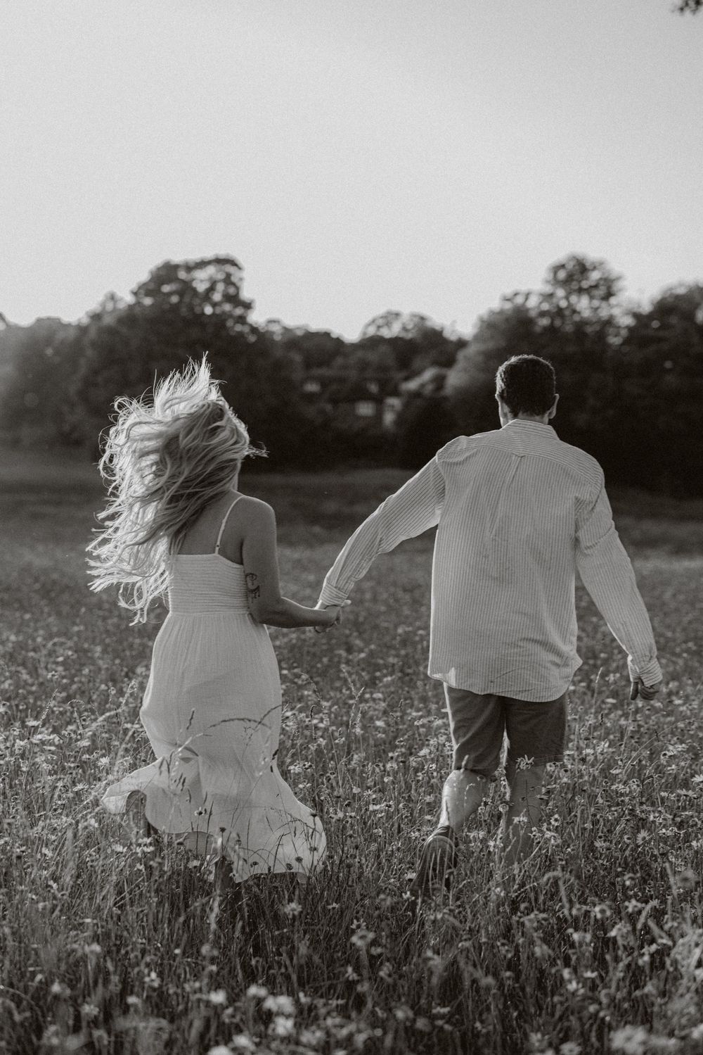 Black and white photo of couple running through wildflower meadow with flowing dress movement.
