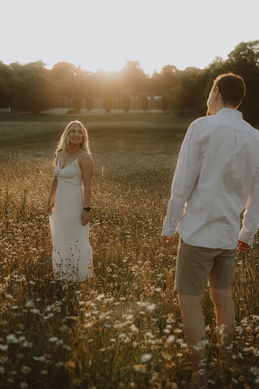 Romantic couple standing in a golden wildflower meadow at sunset with warm backlighting.