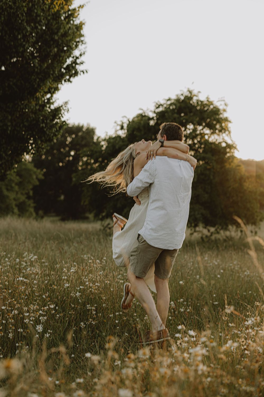 Playful couple embracing and spinning in a sunlit meadow with wildflowers.