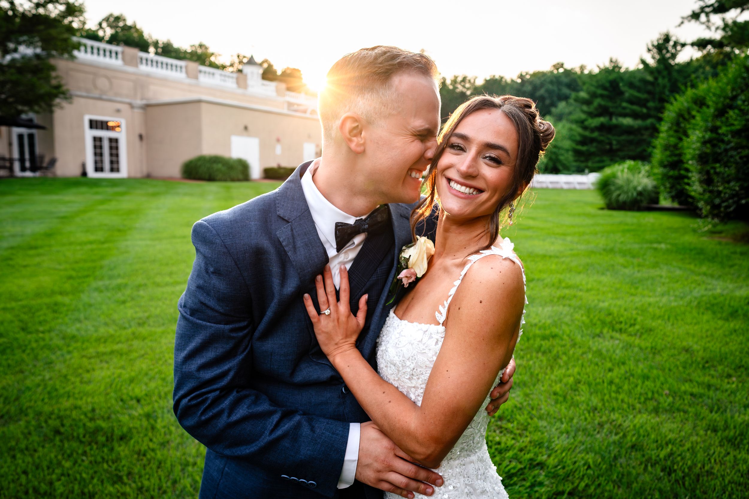 Newlyweds share intimate moments on manicured lawn during golden hour photography session.