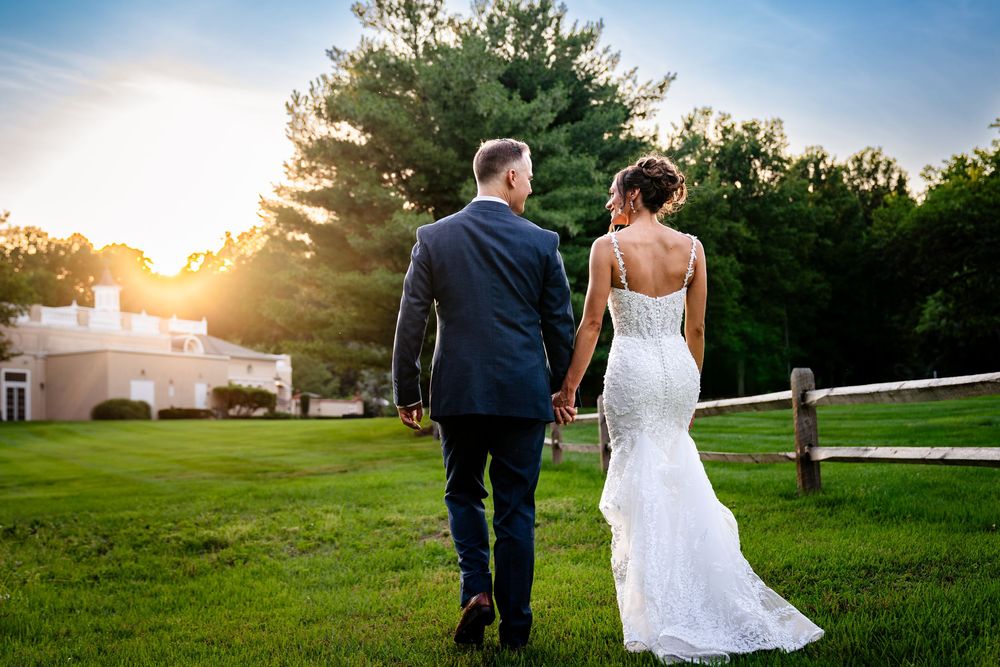 Wedding couple walks through a scenic garden path at sunset with golden light filtering through trees.