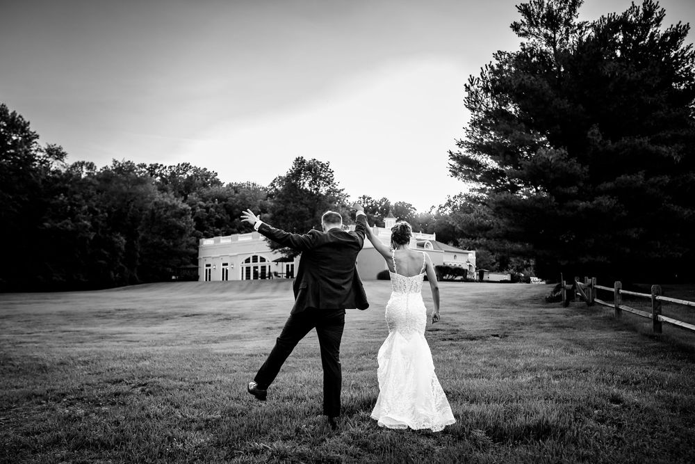 Black and white photo of a couple walking across a grassy field at their wedding.