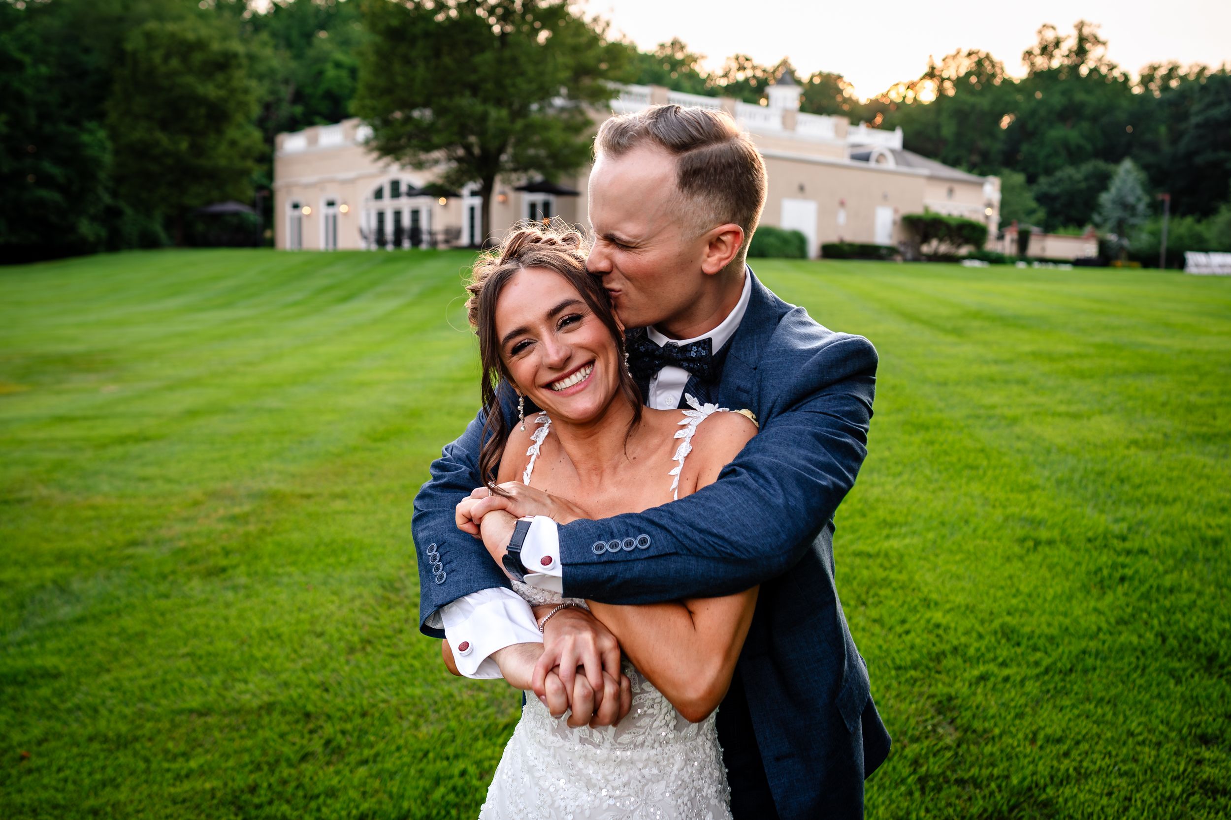 Couple shares a playful moment on a lush green lawn during their wedding celebration.
