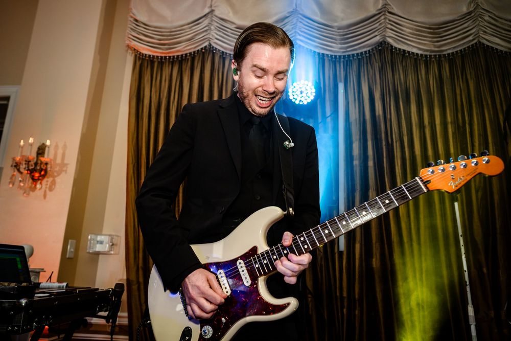 Musician plays electric guitar on stage at wedding reception with blue lighting.