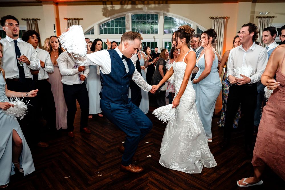 Wedding guests dancing and celebrating on a wooden dance floor at reception.