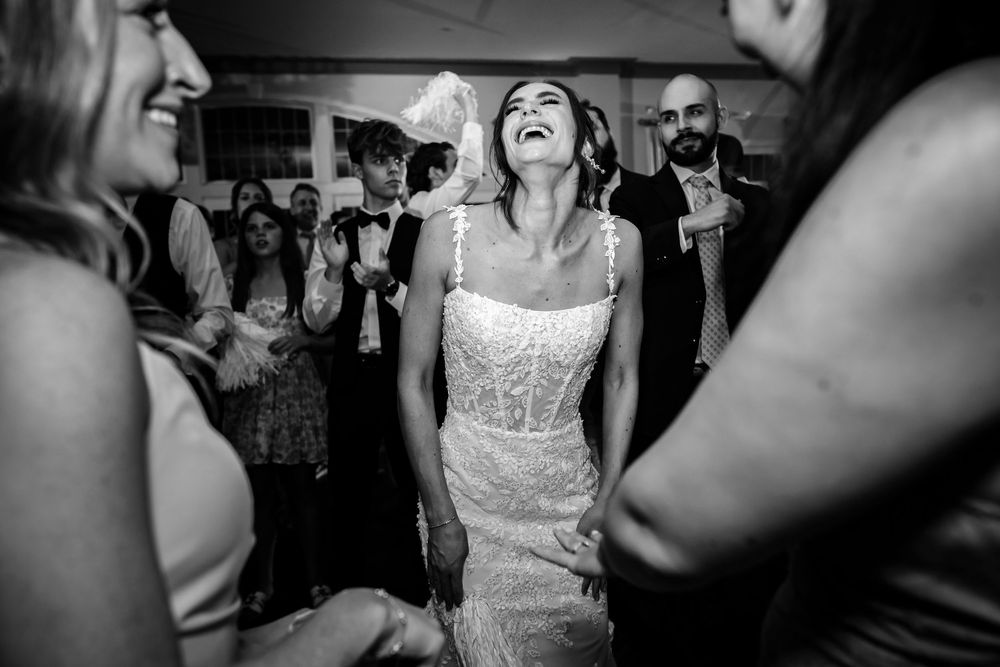 Wedding reception guests dancing and celebrating on a crowded dance floor with colorful lighting.