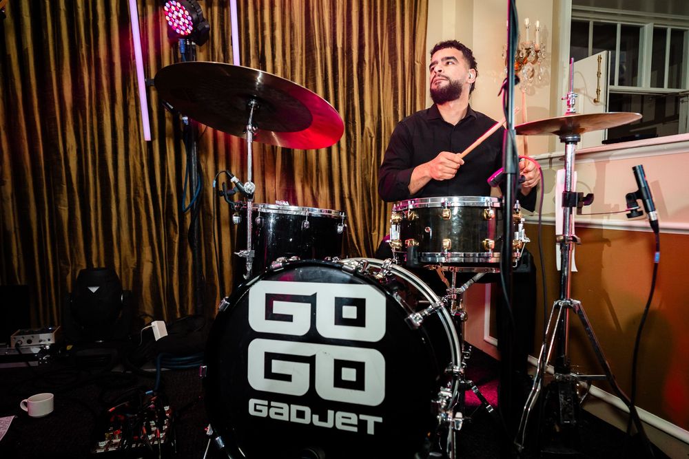 Band performing on stage with instruments and lighting equipment at an indoor venue.