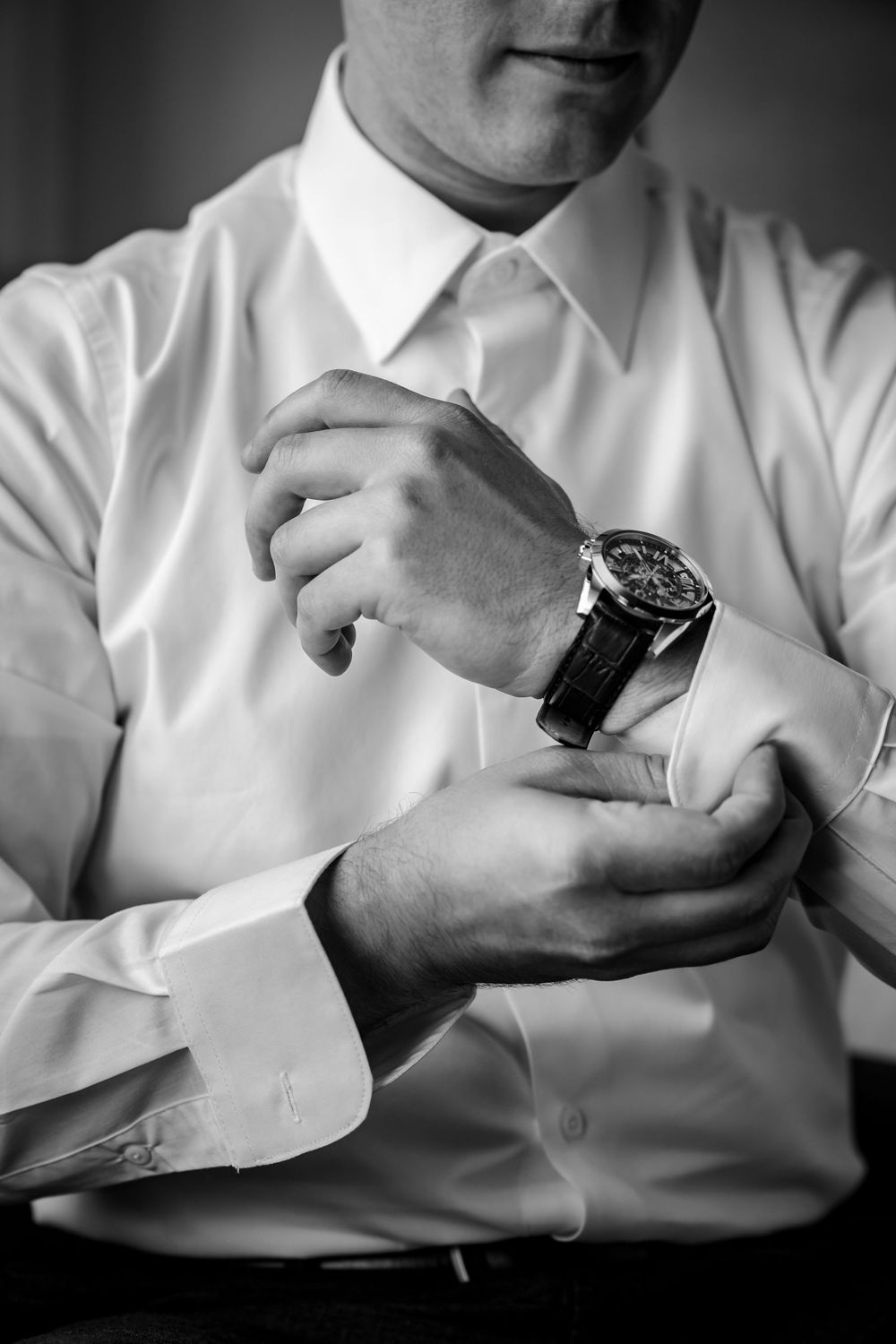 Black and white photo of hands adjusting a luxury watch with white dress shirt cuffs.
