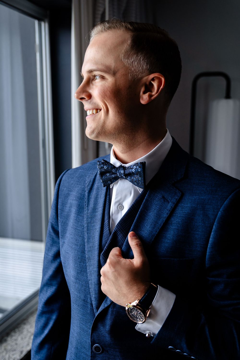Side profile of person in navy suit with bow tie looking out window.