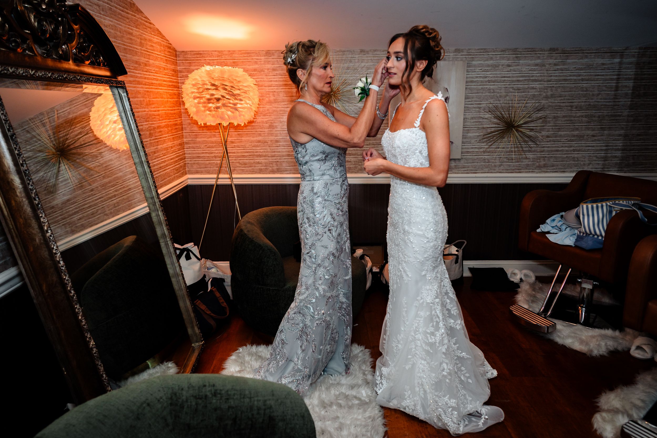 Two people in elegant lace wedding gowns share an emotional moment together in a dimly lit room.