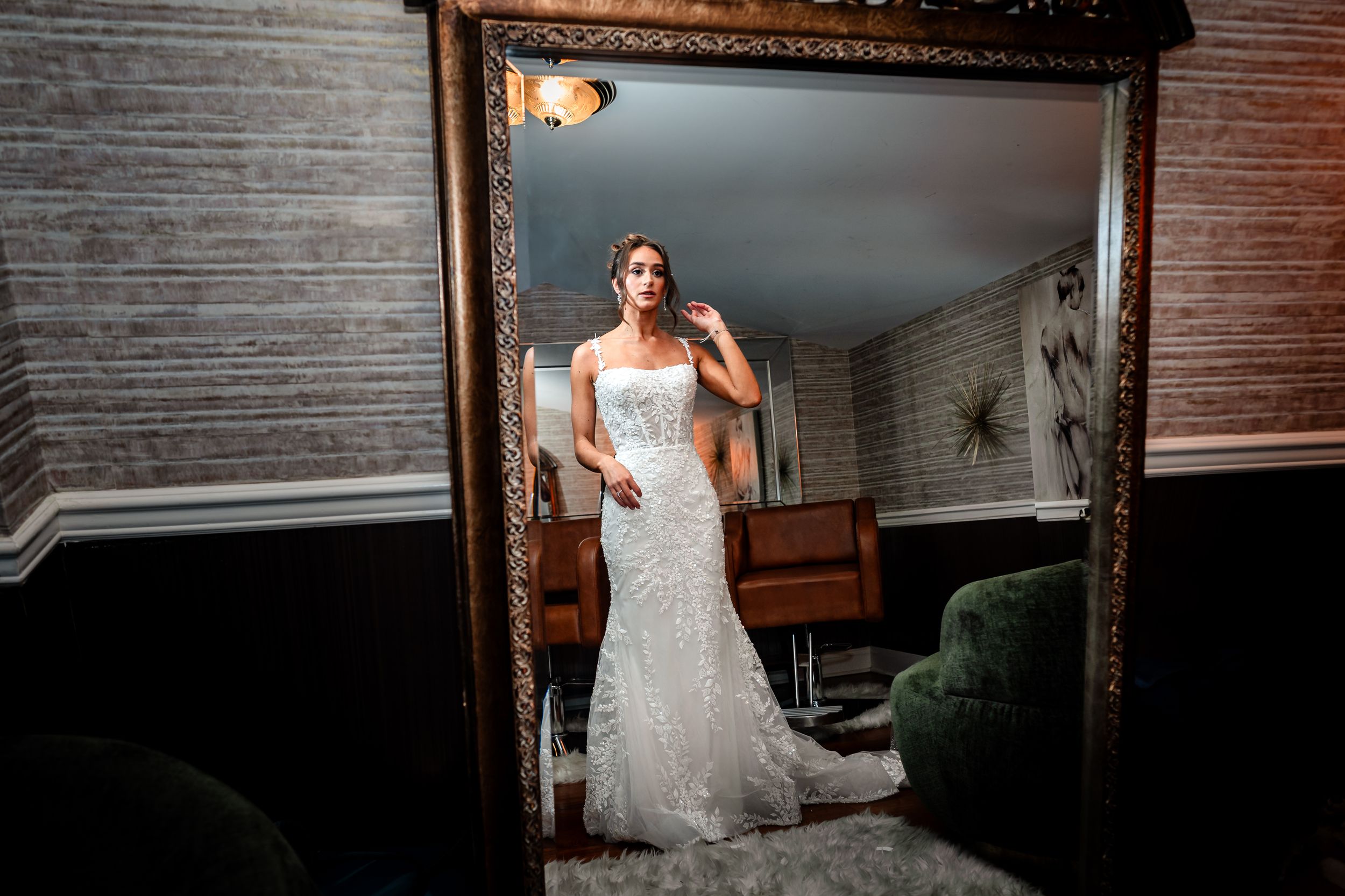Reflection of bride in white lace wedding dress posing in ornate gold mirror.