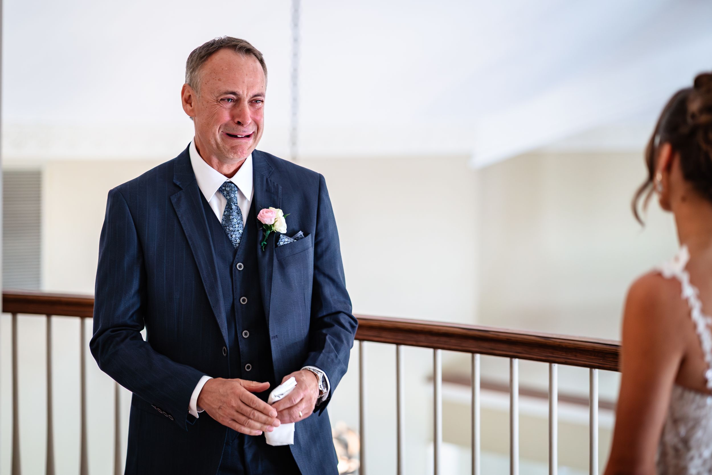A person in a navy suit with boutonniere stands in a bright indoor setting.