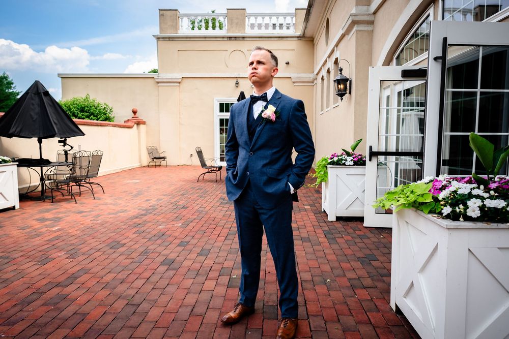 A person in a navy suit stands on a brick patio outside an elegant venue.