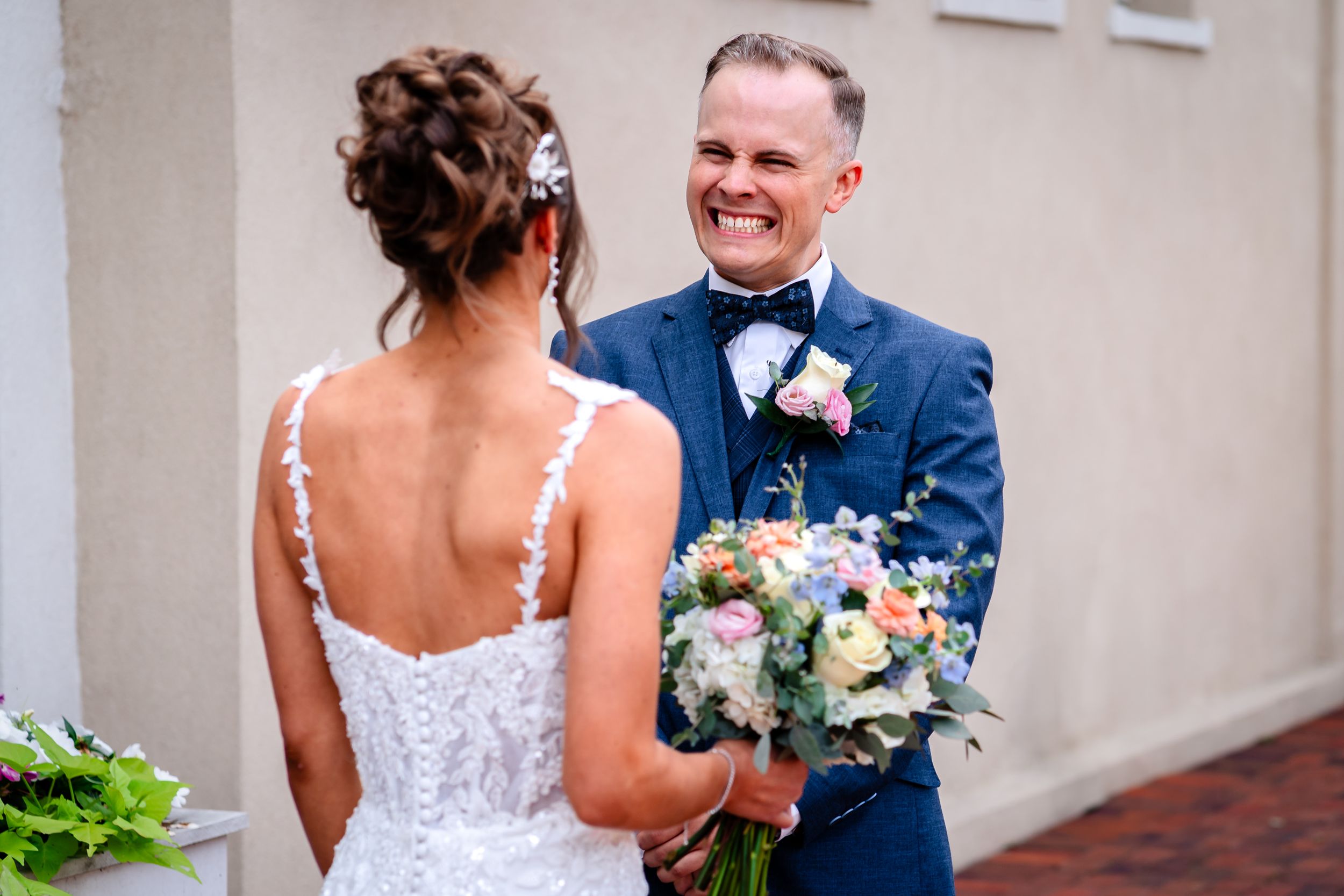 Couple in wedding attire smiling together against a neutral colored wall.