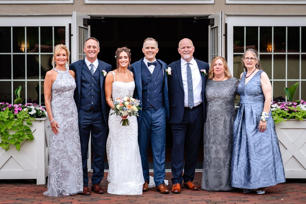 Wedding party members in navy suits and light blue dresses line up for formal portraits.